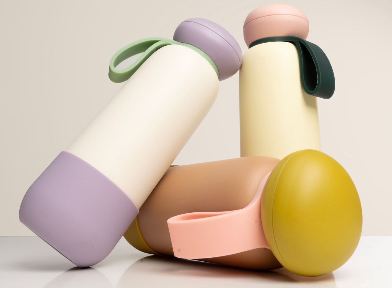 Four pastel-colored insulated water bottles with silicone handles on a white minimalist background.