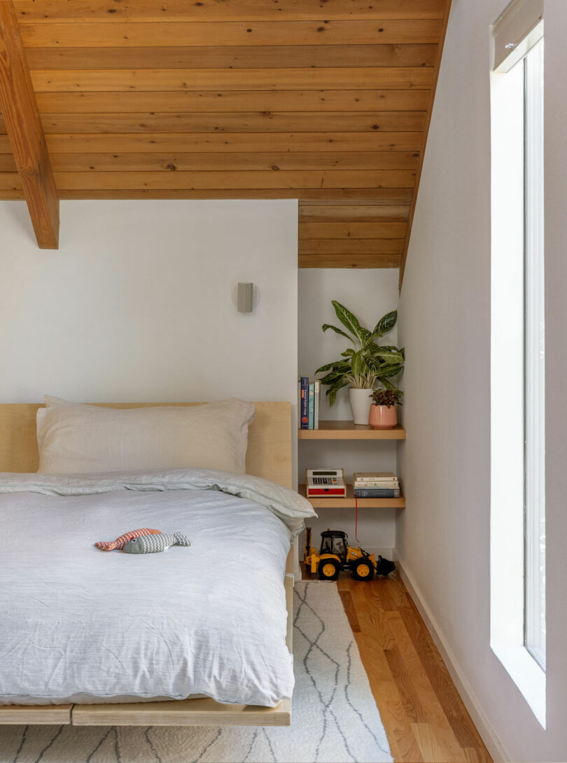 Minimalist bedroom with a wooden platform bed and natural light from high windows.