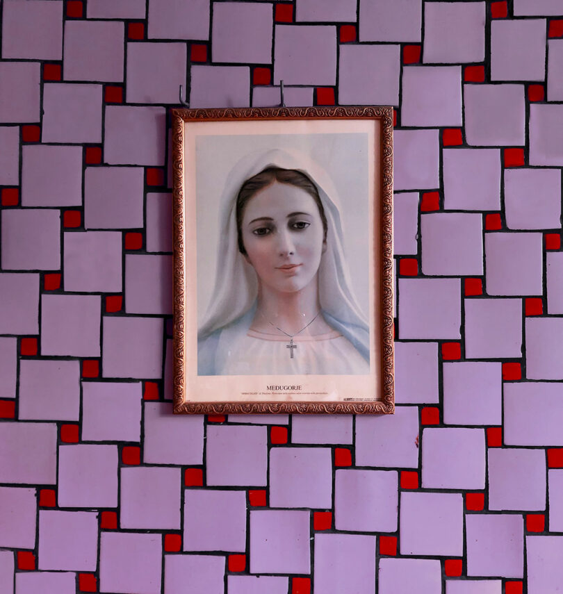 A framed religious portrait of the Virgin Mary against a red and purple geometric wallpaper.
