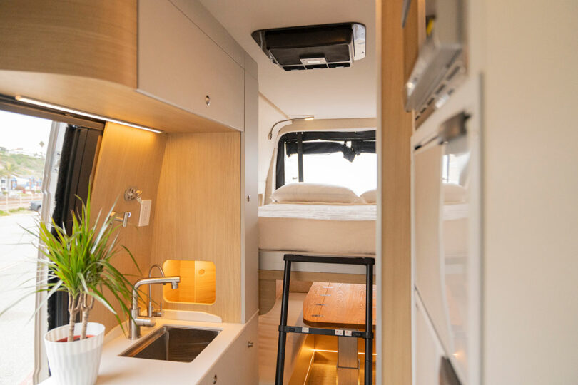 Interior view of a camper van showing the high ceiling, loft bed, and Scandinavian-style wood finishes.