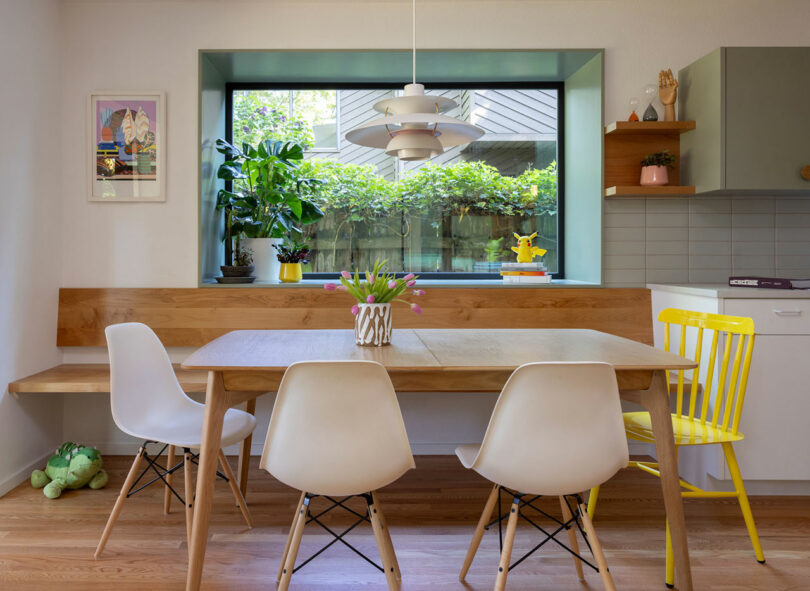 Dining area with a built-in wooden bench and modern chairs next to a large window.