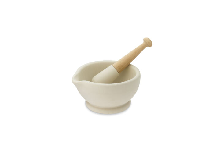 A cream-colored ceramic mortar and wooden pestle set against a neutral background in a minimalist style.