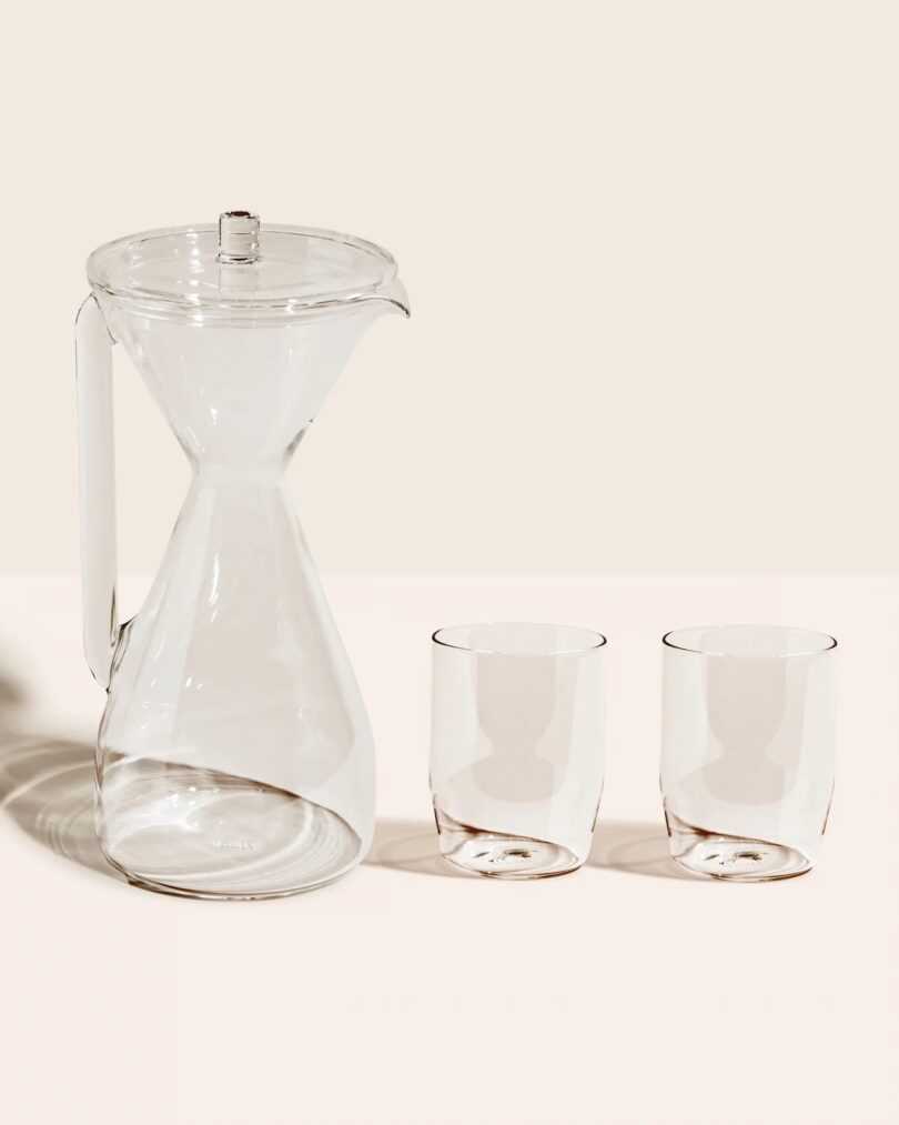 A clear glass pour-over carafe standing next to two matching double-walled glasses.
