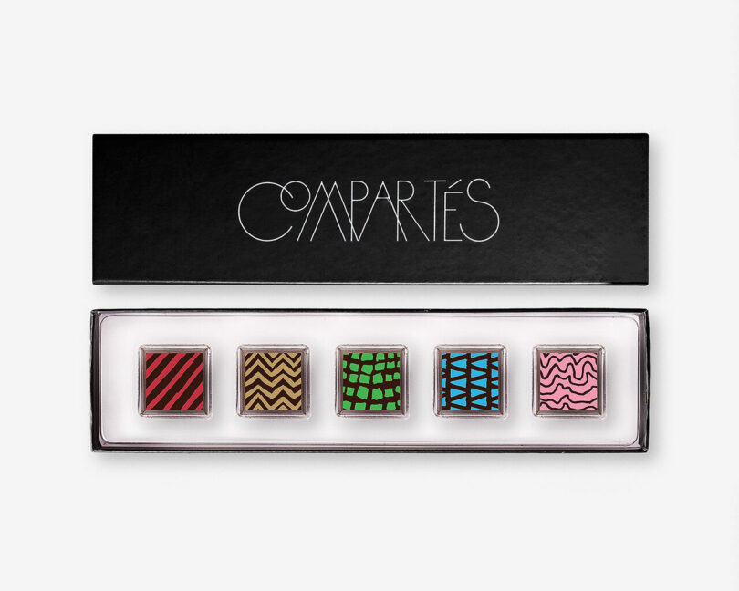 A black box containing five chocolate truffles, each featuring a different colorful geometric design.