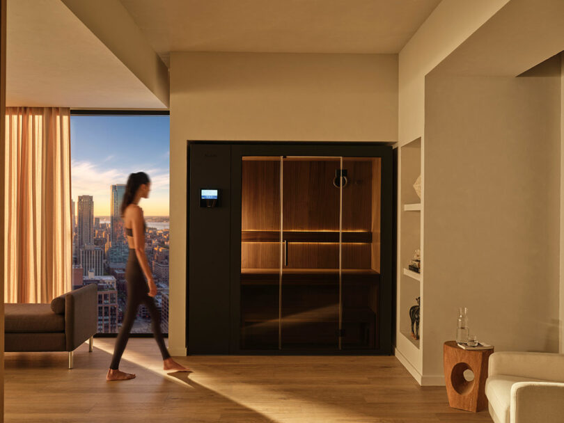 A person walking past a built-in KLAFS sauna in a contemporary living room.