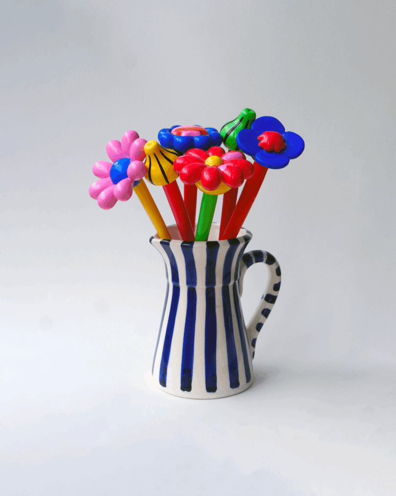 A white ceramic pitcher with blue stripes holding flower-topped pens.