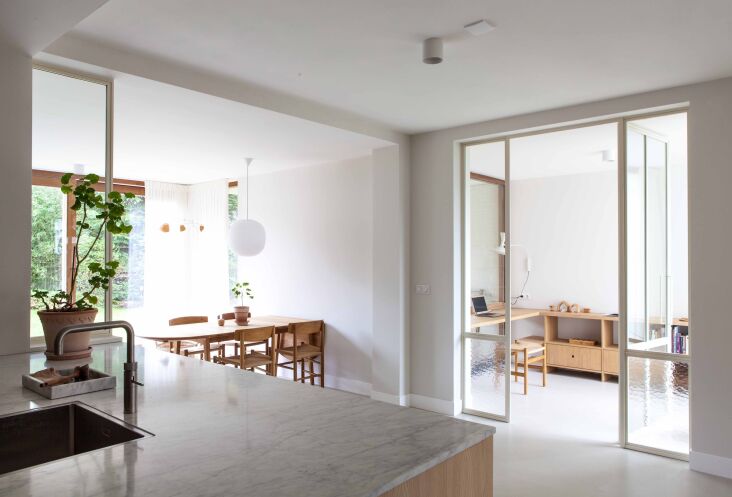 An open-plan kitchen and dining area featuring a glass partition that leads to a home office.