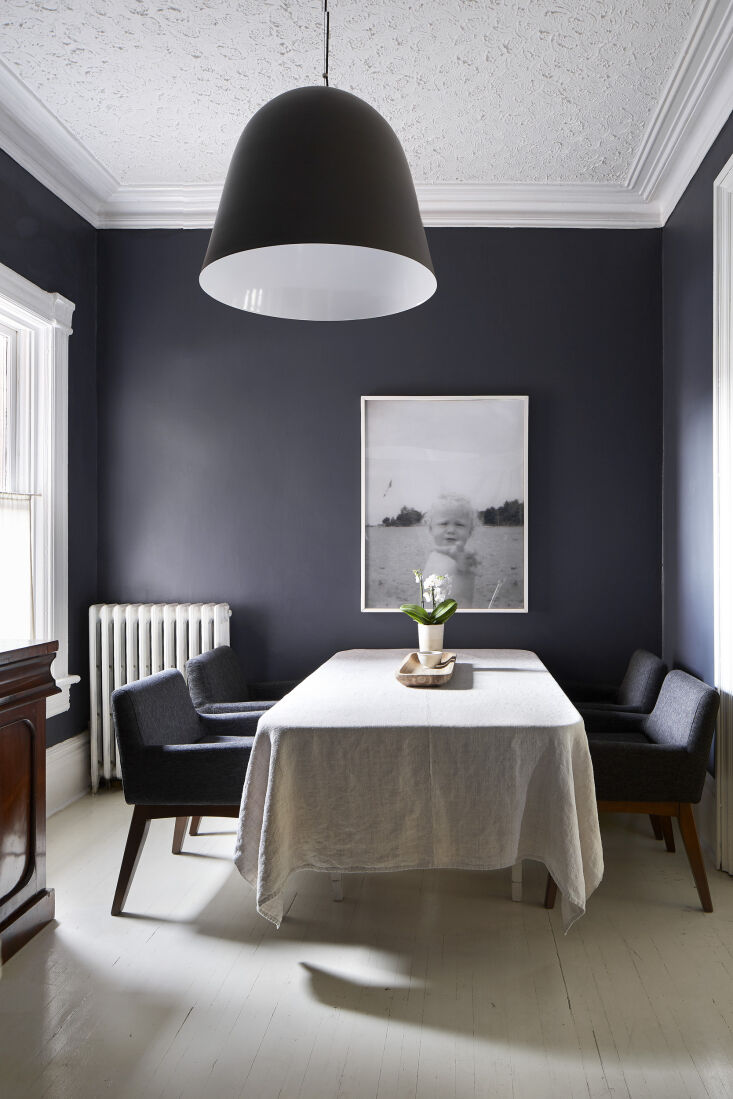 A dark, moody dining room with black walls and a modern pendant light.