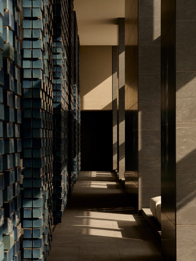 Geometric shadows cast across a textured blue wall and gray tiled floor in a minimalist hallway.