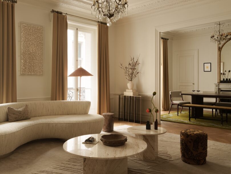 A neutral-toned living room with a curved sofa and marble coffee tables under a classic chandelier.