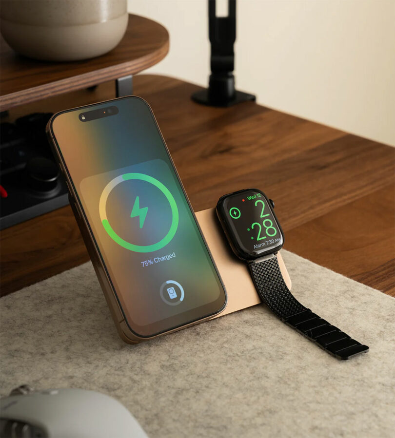 An iPhone and Apple Watch charging simultaneously on a gold-colored Kuxiu charging stand on a desk.