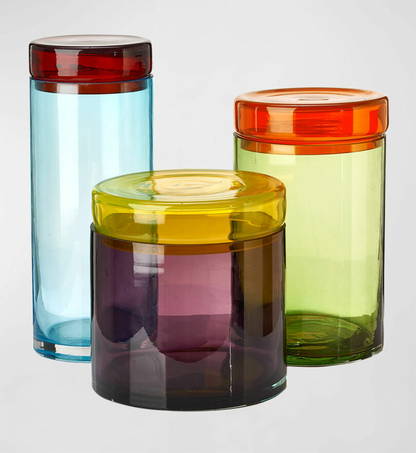 Mouth-blown glass jars in blue, purple, and green with contrasting red and yellow lids.