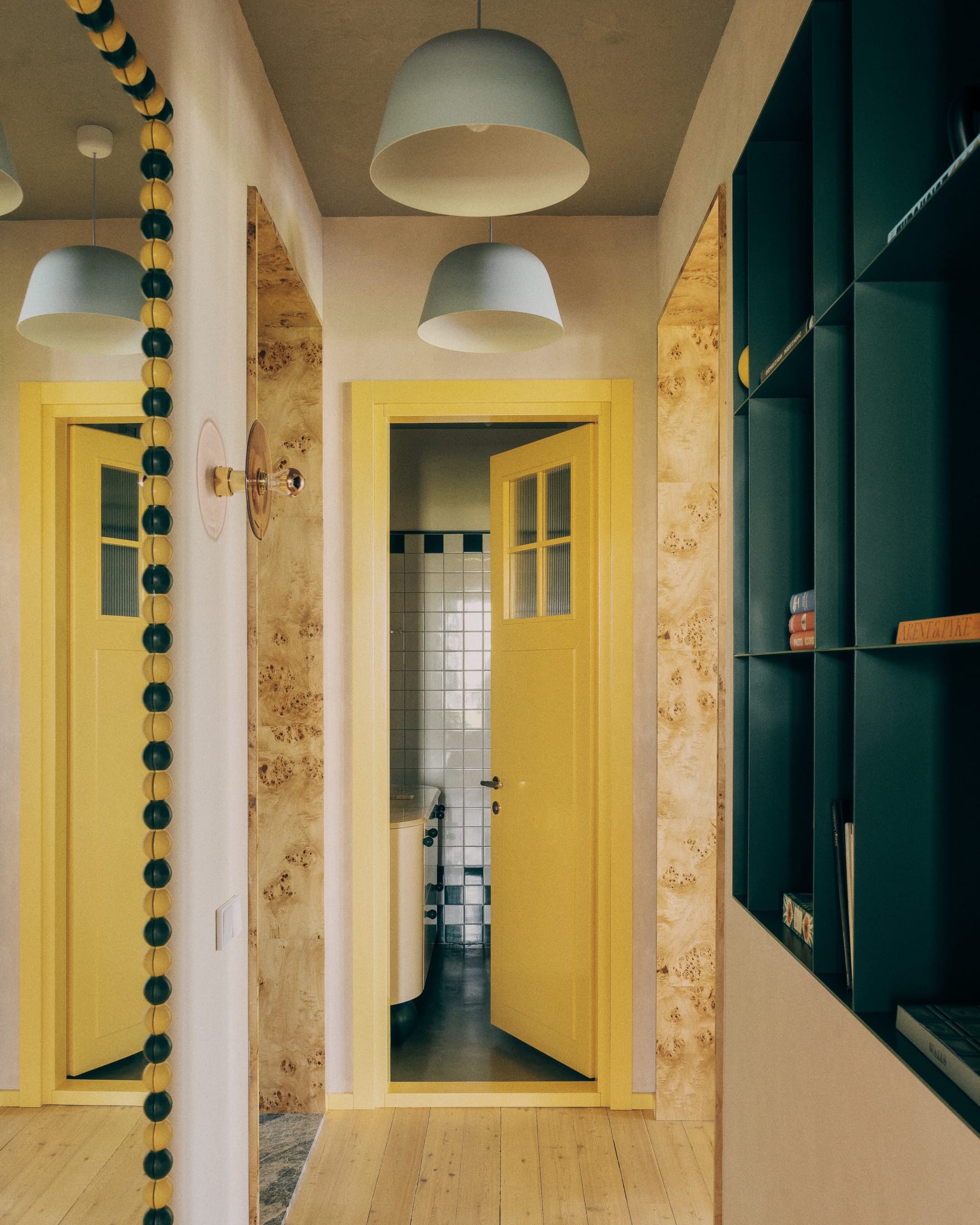 A modern hallway featuring vibrant yellow doors, teal built-in shelving, and burl wood accents.