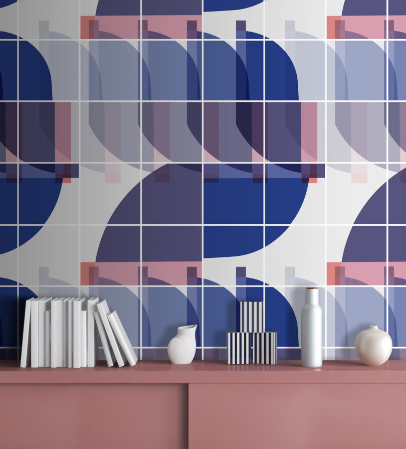 Geometric wallpaper in soft tones above a pink shelf with books and decorative items.
