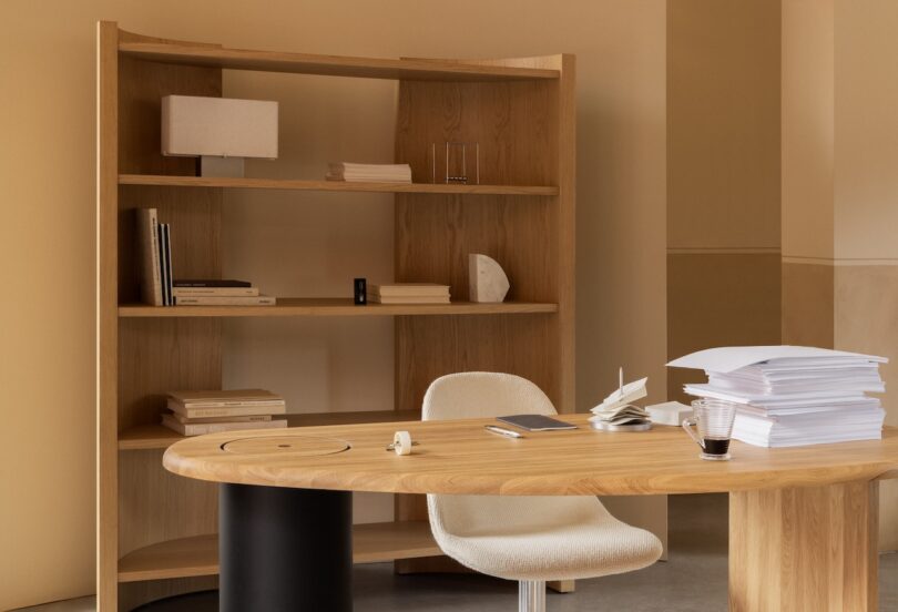 A tall oak Crescent bookshelf styled with books and objects in a minimalist home office.