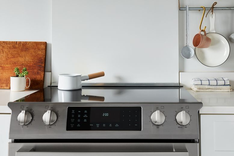 Modern stainless steel electric range in a minimalist Scandinavian style kitchen with white cabinets.