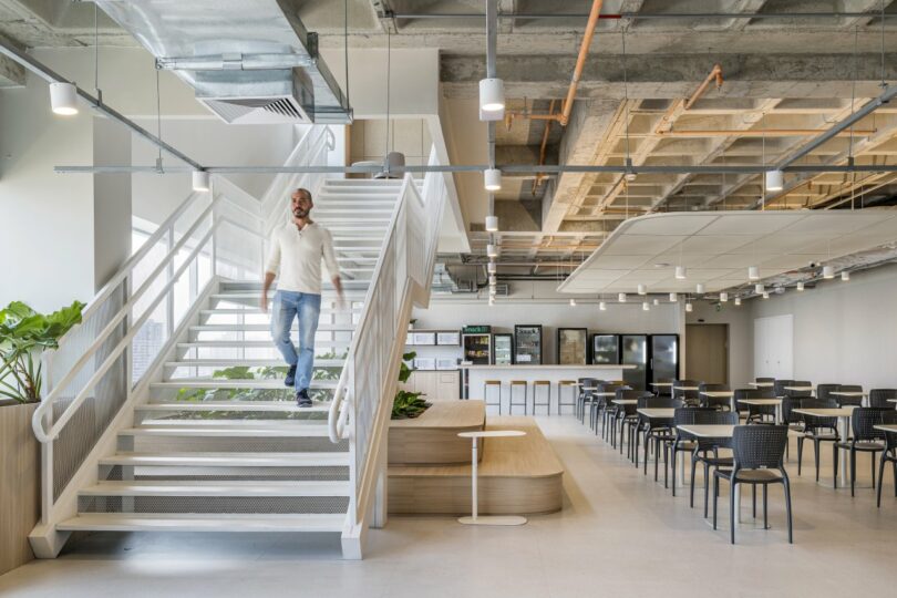 An industrial-style office dining area with a prominent white staircase and exposed concrete ceilings.