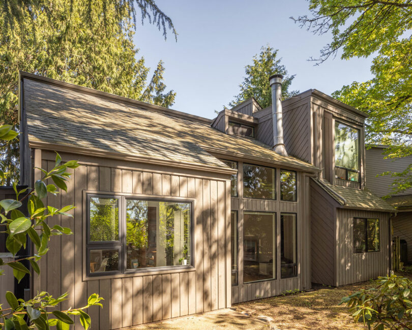 Exterior view of a modern wood-sided house with a gabled roof and large windows nestled in trees.