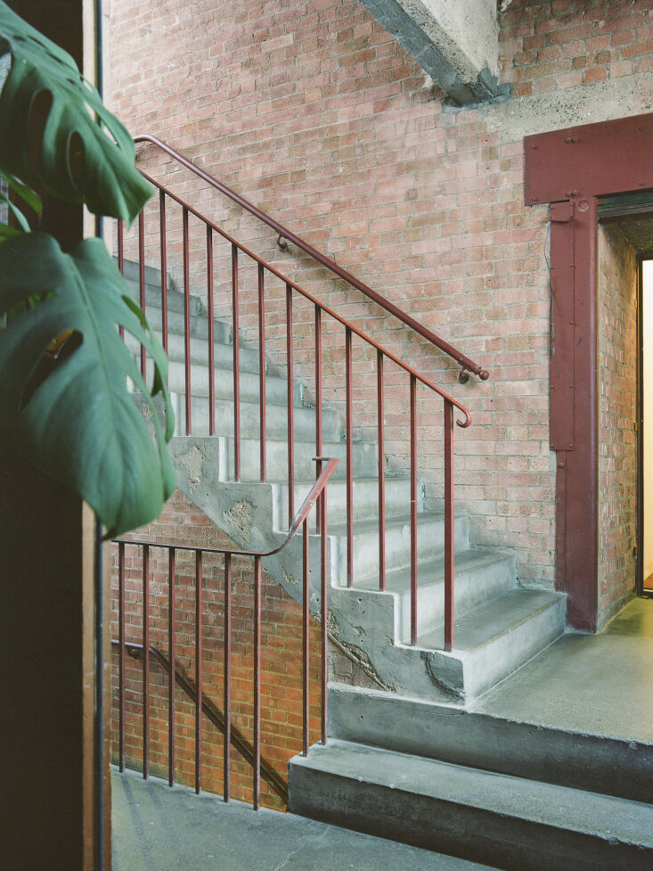 Industrial stairwell with exposed brick, concrete steps, and rust-colored metal railings.