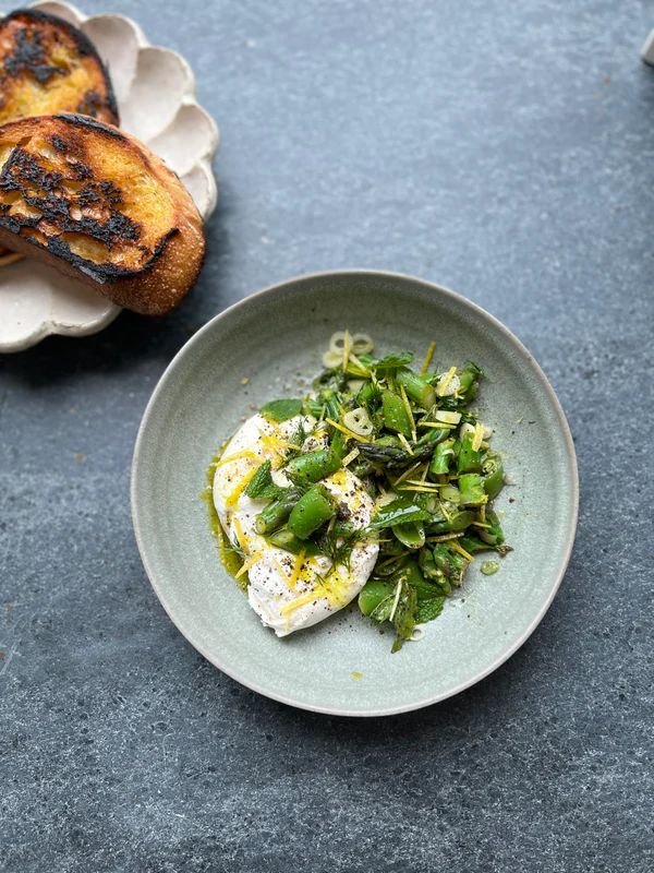 A close-up of the completed spring salad featuring creamy burrata and bright green vegetables.