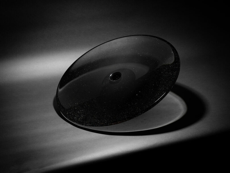 A transparent glass disc with a central indentation casting a sharp shadow through light refraction.