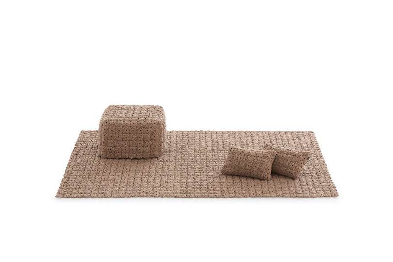 A camel-colored woven rug paired with matching pillows and a cube-shaped pouf.