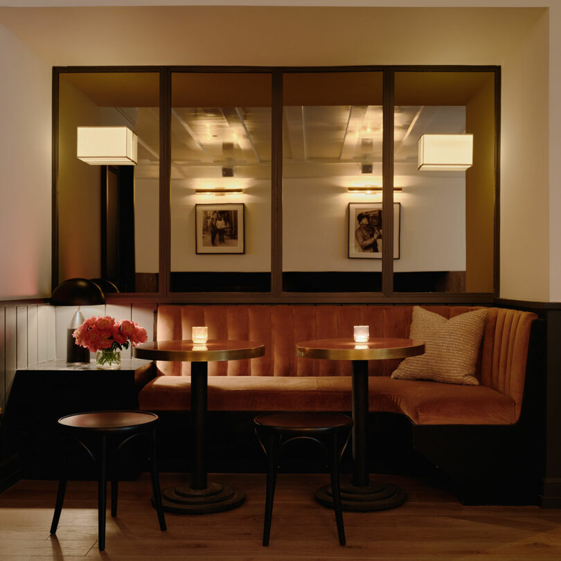 A cozy seating area with orange velvet booths and round wooden tables reflected in wall mirrors.