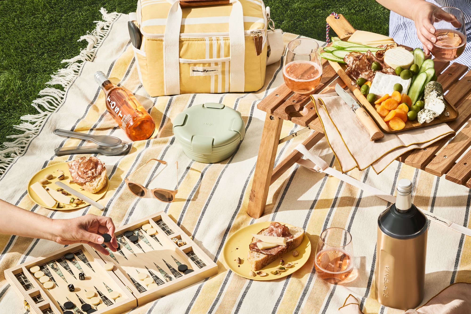 A curated selection of picnic essentials being placed into a modern basket.