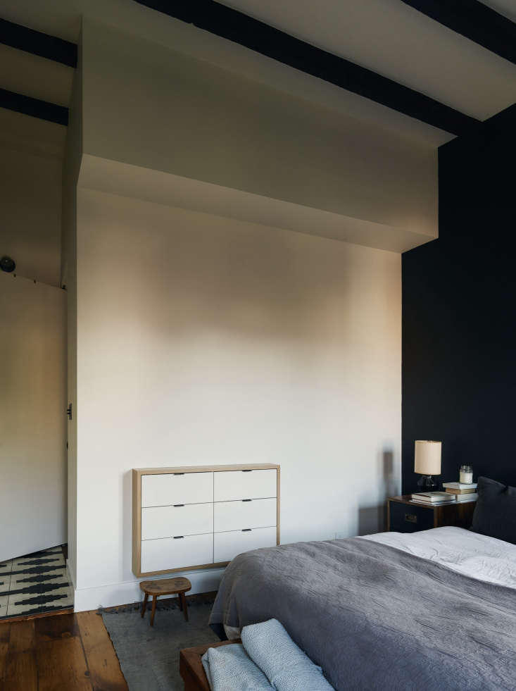 Modern bedroom with a white recessed dresser built into a dark accent wall with exposed beams.