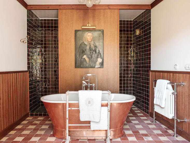 A luxury bathroom featuring a historic female portrait overlooking a freestanding bathtub in a Spanish hotel.