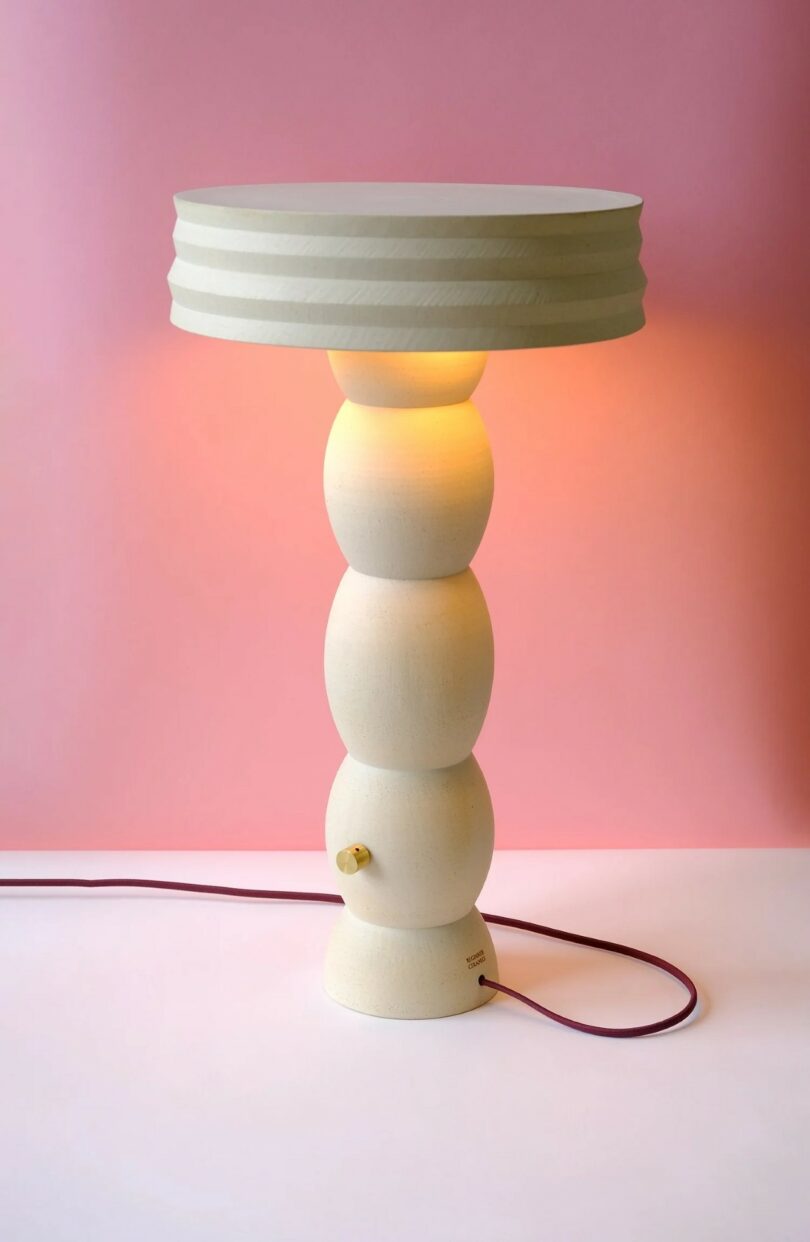 A modern off-white stacked ceramic lamp with a ridged shade on a pink background.