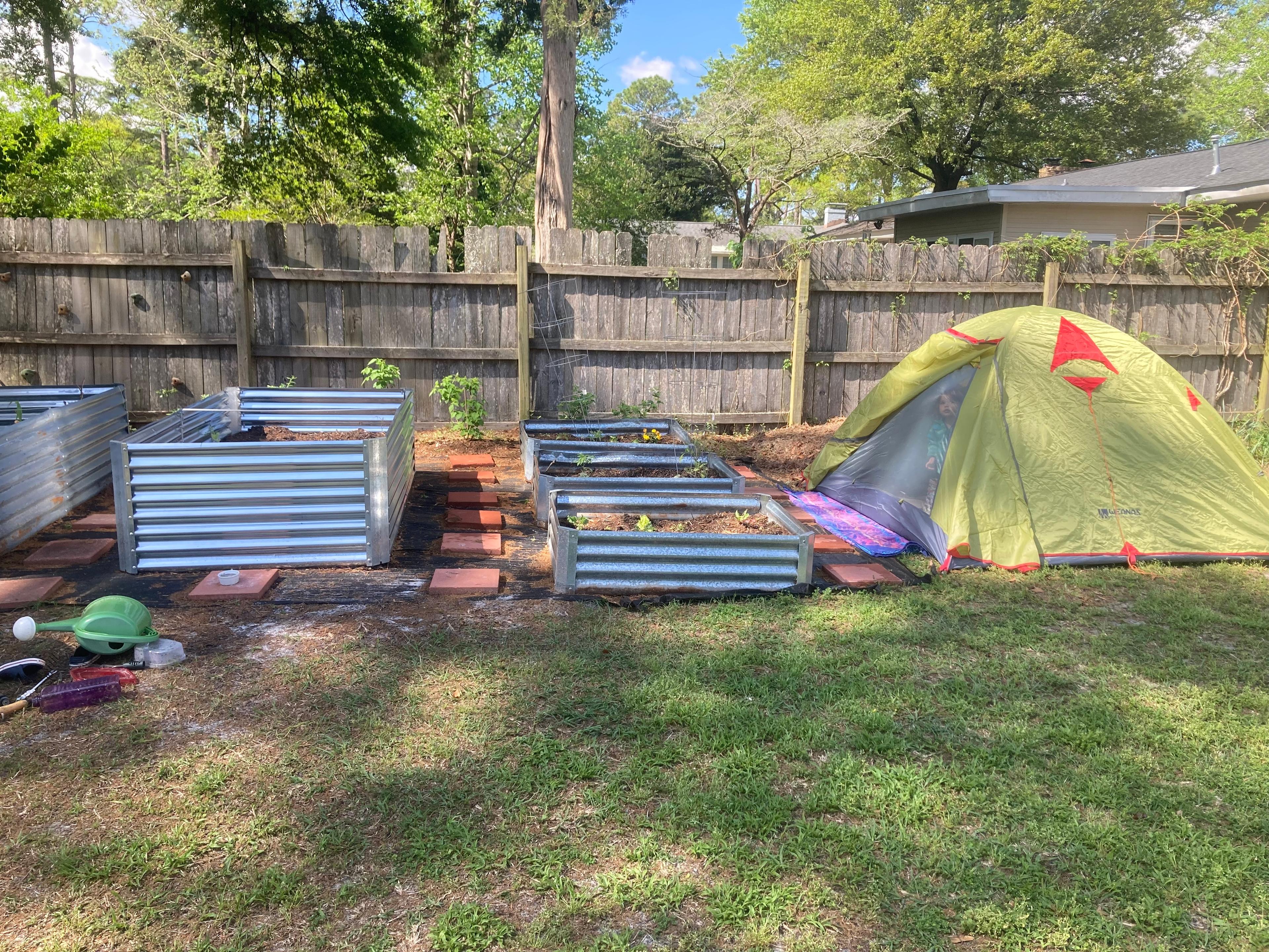 A small play tent set up in a backyard garden area surrounded by vegetable beds.