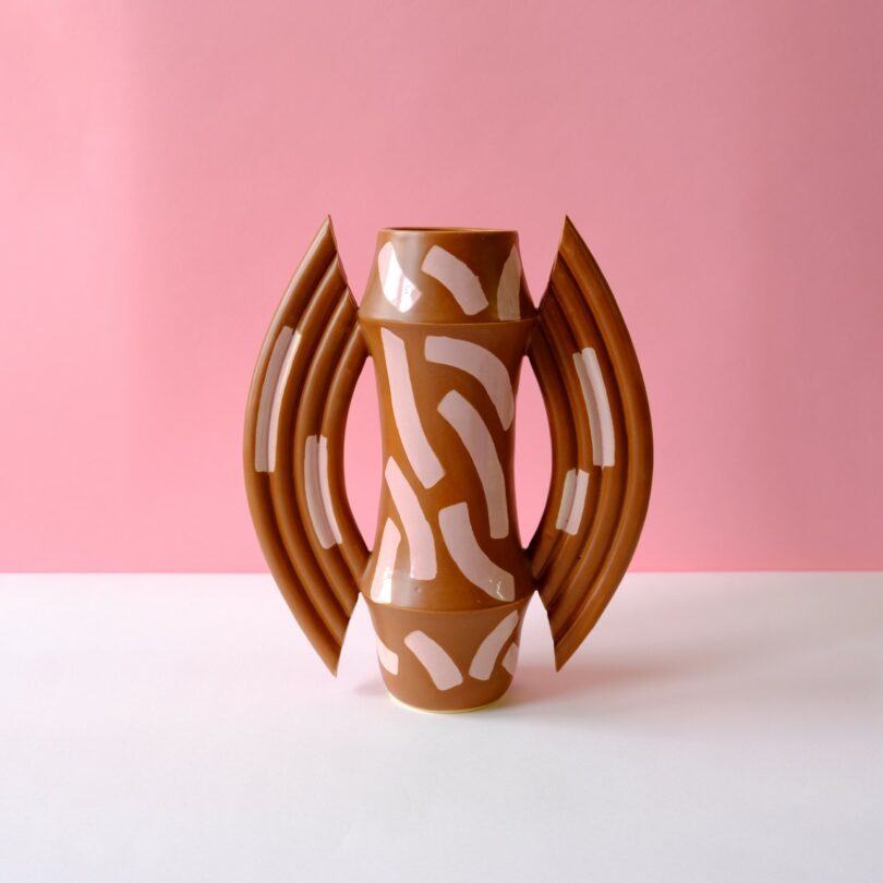 A brown ceramic vase with symmetrical handles and abstract white painted patterns.