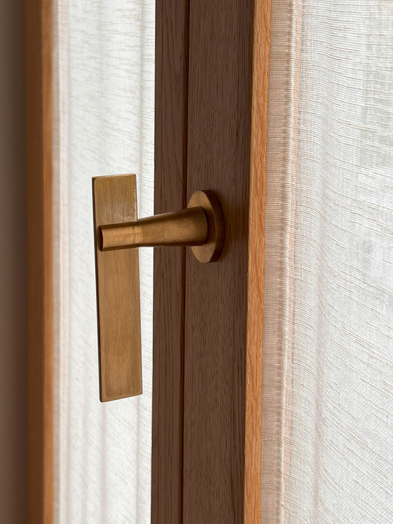 Close-up of a eucalyptus wooden door with a brass handle and a soft sheer curtain.