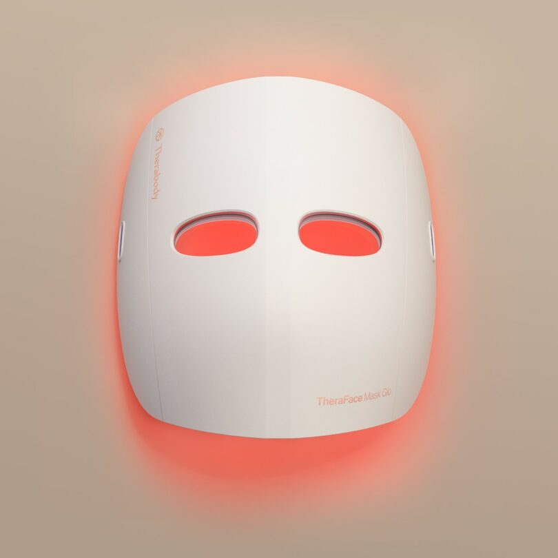 A white minimalist LED facial mask glowing with red light therapy.