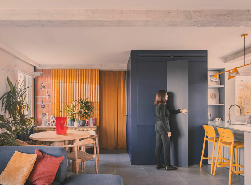 A person standing by a large blue sculptural cabinet that serves as a room divider in a colorful apartment.