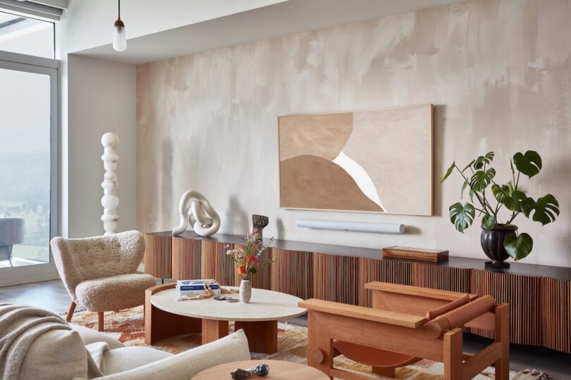 A close-up of a living room featuring a textured beige armchair, wooden low cabinet, and sculptural ceramic decor.