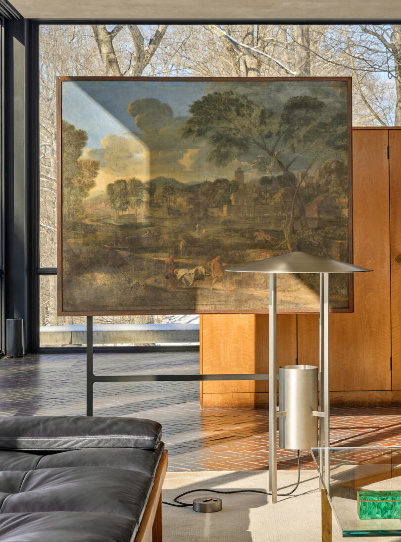 The 1953 floor lamp standing in a modern living room next to a large landscape painting and wood paneling.