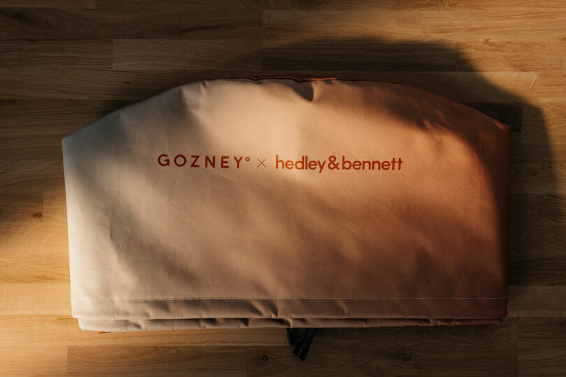 A folded fabric oven cover featuring the Gozney and Hedley & Bennett logos.