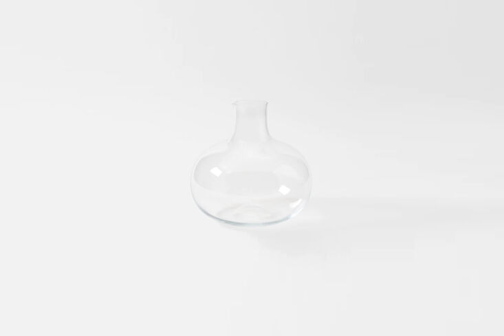 A large clear glass vase holding simple botanical branches on a coffee table.