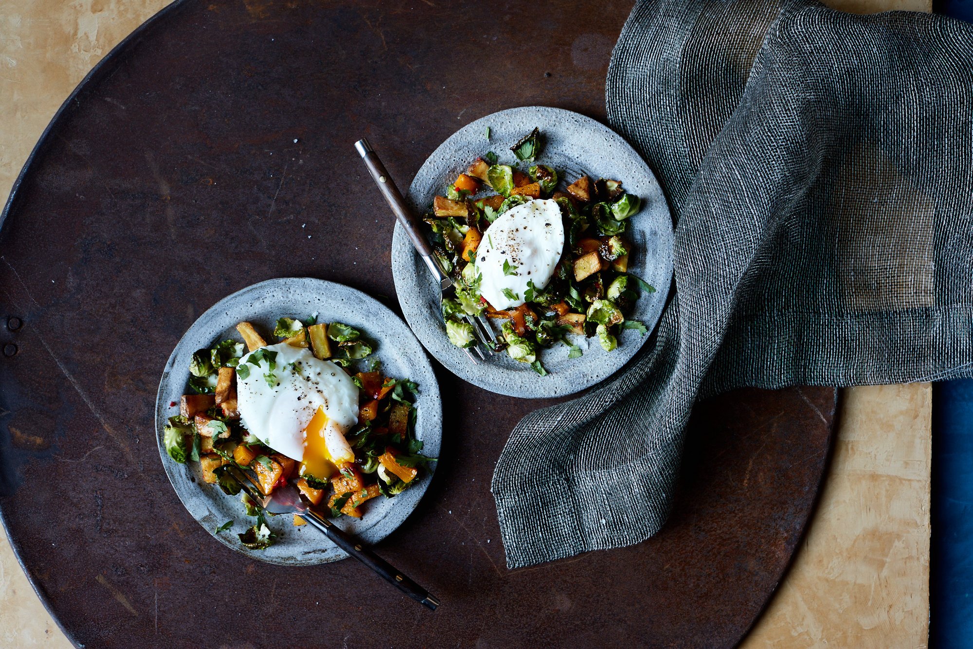 Close-up of roasted pumpkin chunks and crispy Brussels sprout leaves topped with a runny poached egg.