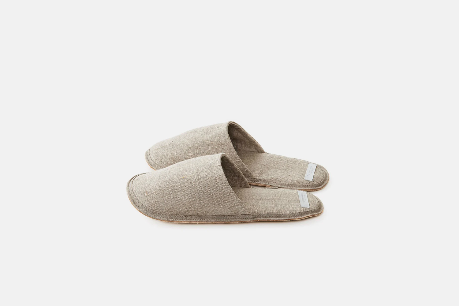 A pair of natural linen slippers on a wooden floor.
