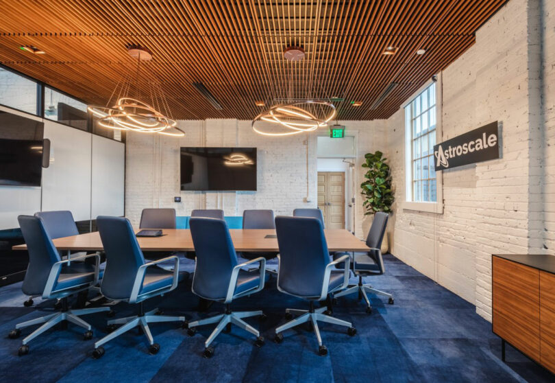 Astroscale logo on a white brick wall in a conference room with modern blue chairs.