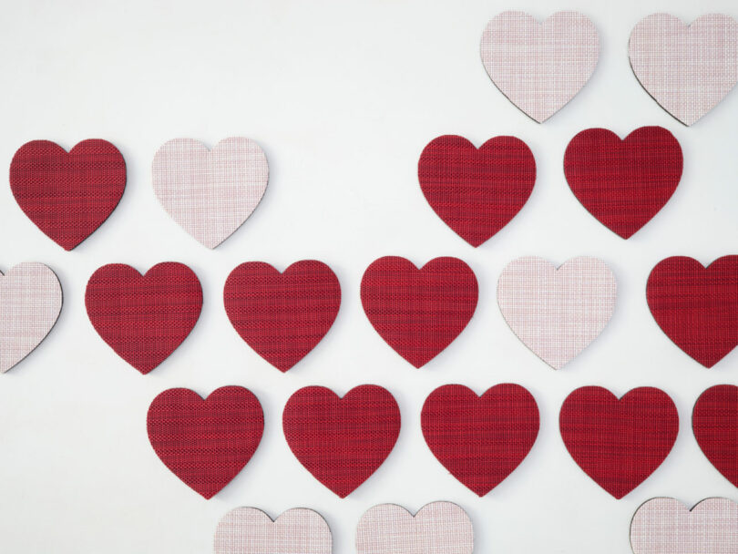 A pattern of red and pink heart shapes in a textured weave style on a white background.