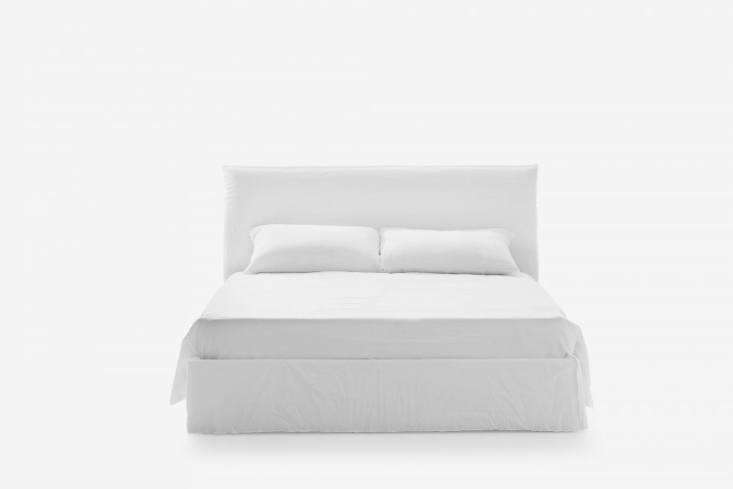 A white slipcovered bed with a soft, rounded silhouette in a minimalist bedroom.