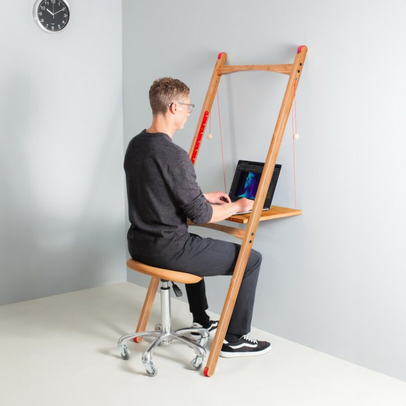A man using a light wood wall-mounted desk in a neutral room with no visible wall attachments.