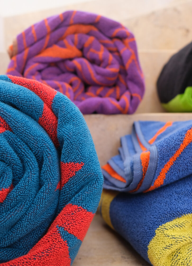Neatly rolled colorful beach towels showcasing various geometric and striped patterns in blue, red, and green.