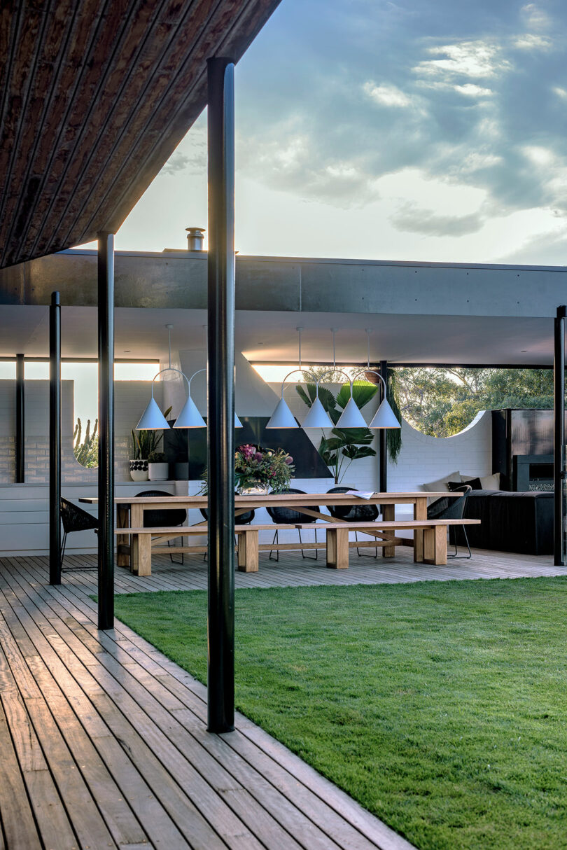 An outdoor dining table under a modern pergola with hanging pendant lights at dusk.