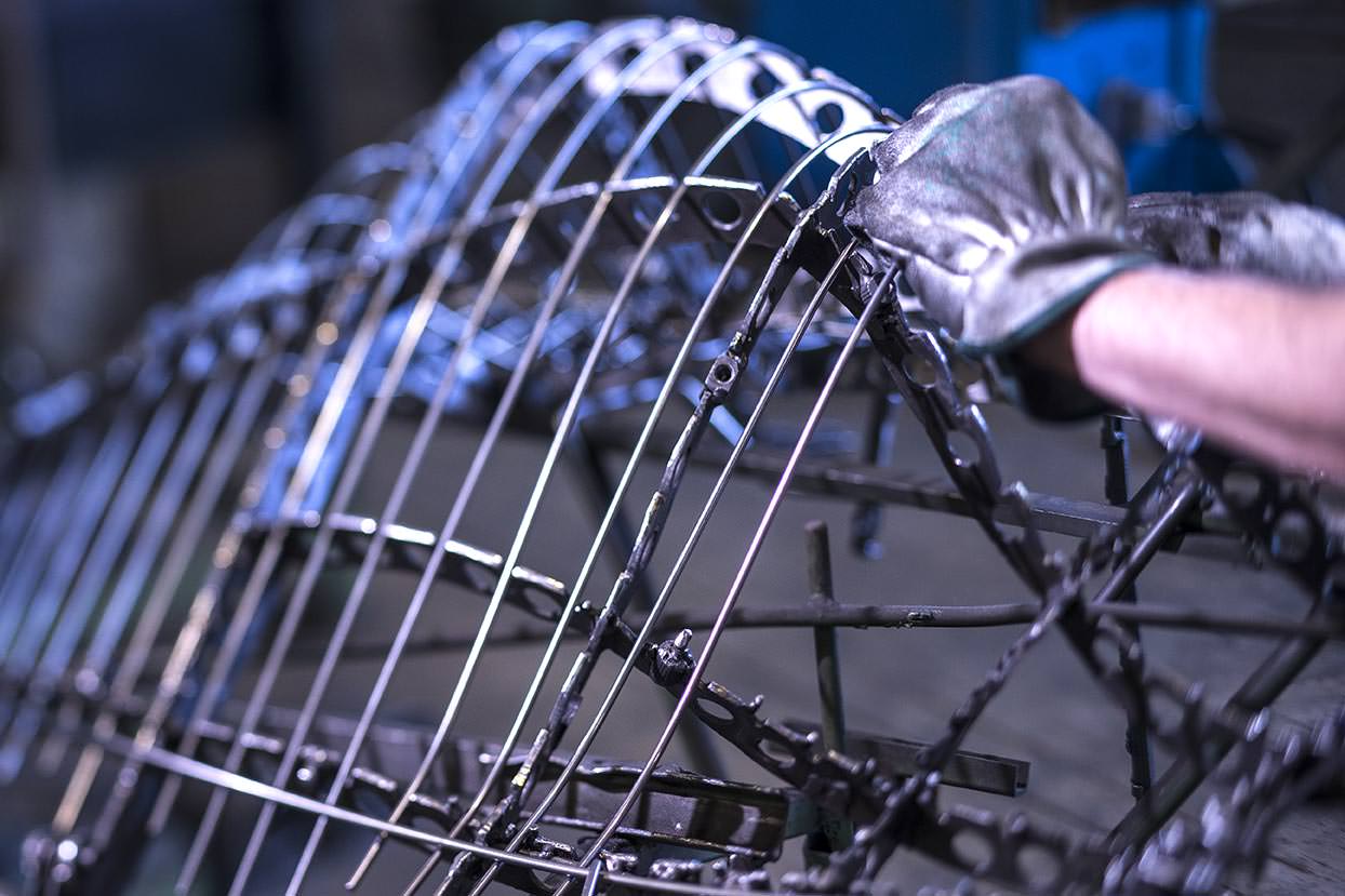 A craftsman working on the manual welding and bending of a metal wire chair frame.