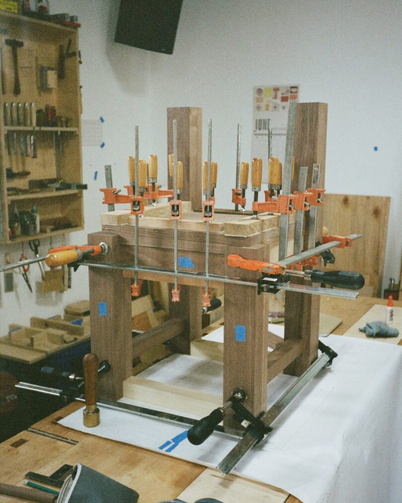 A wooden table frame secured by metal clamps in a woodworking studio.